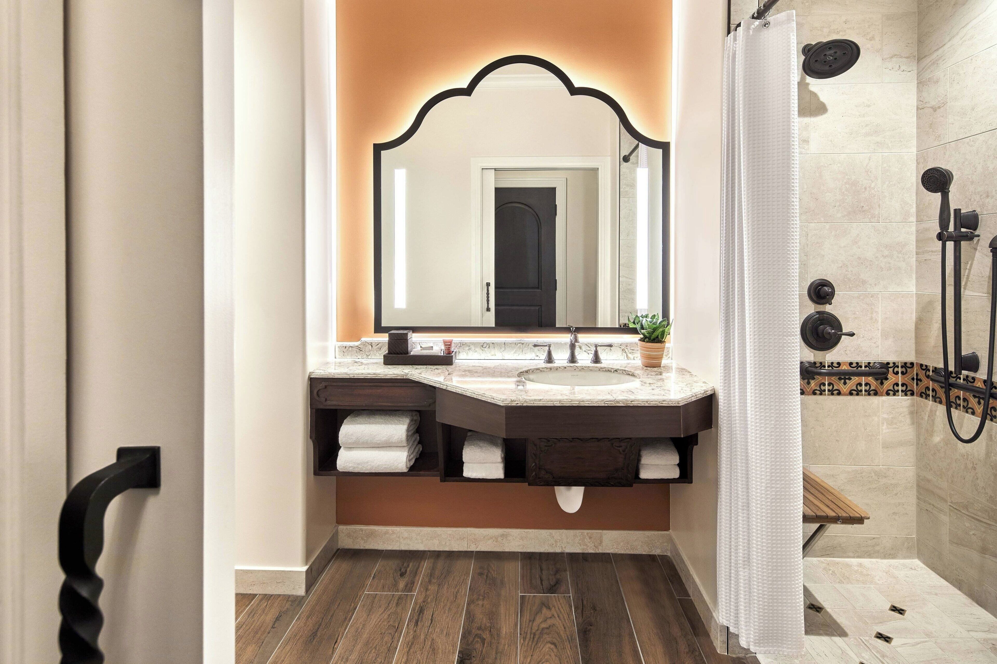 Une salle de bain avec un meuble-lavabo à deux vasques, un grand miroir, un espace douche et un plancher en bois.