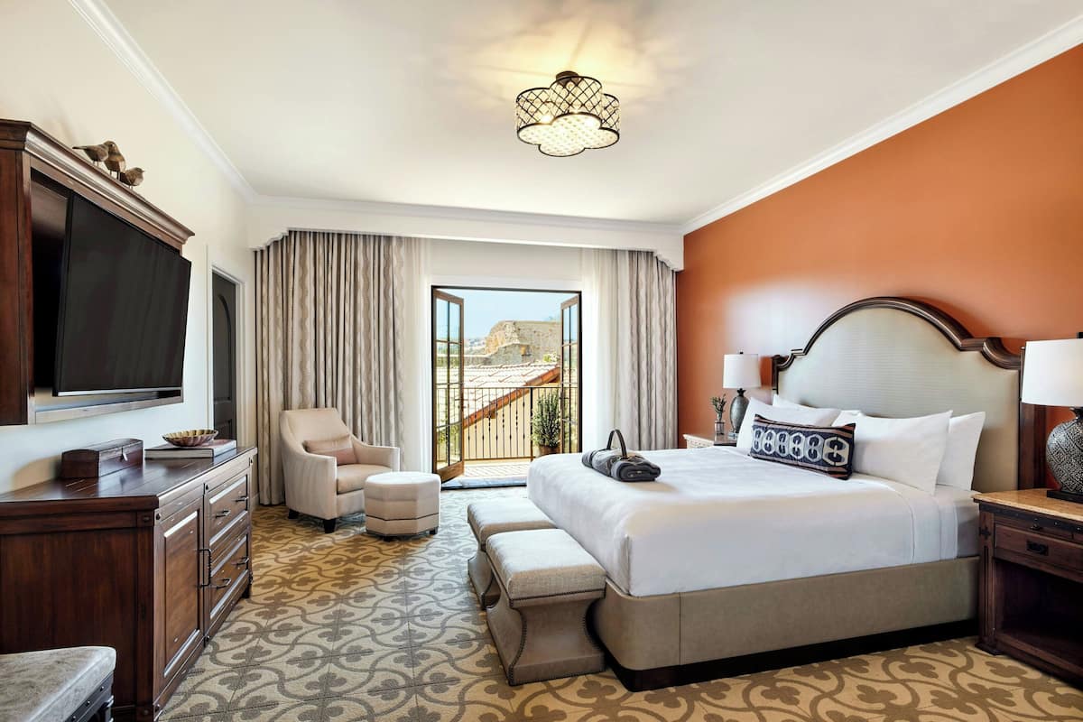 A hotel room with a large bed, a television, a desk, a chair, and a view of the outdoors.
