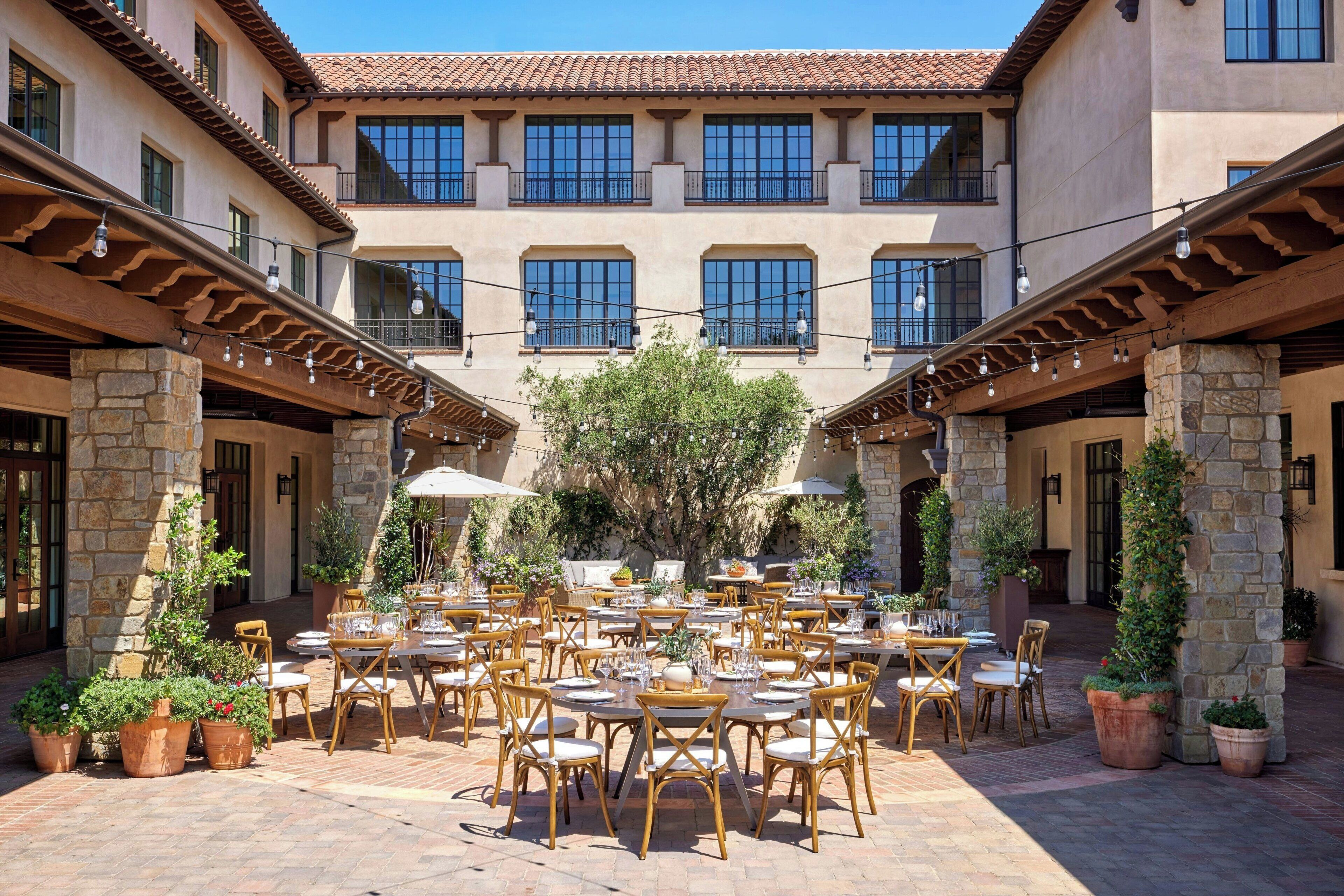 A courtyard with outdoor seating, stone pillars, and a building with multiple windows.
