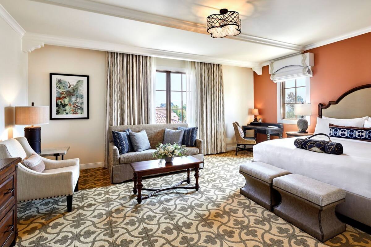 A hotel room with a bed, a sofa, a desk, a chair, and a patterned carpet.