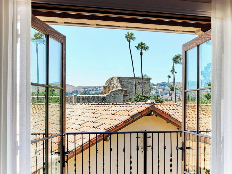 A balcony with a view of a tiled roof, palm trees, and a stone structure.
