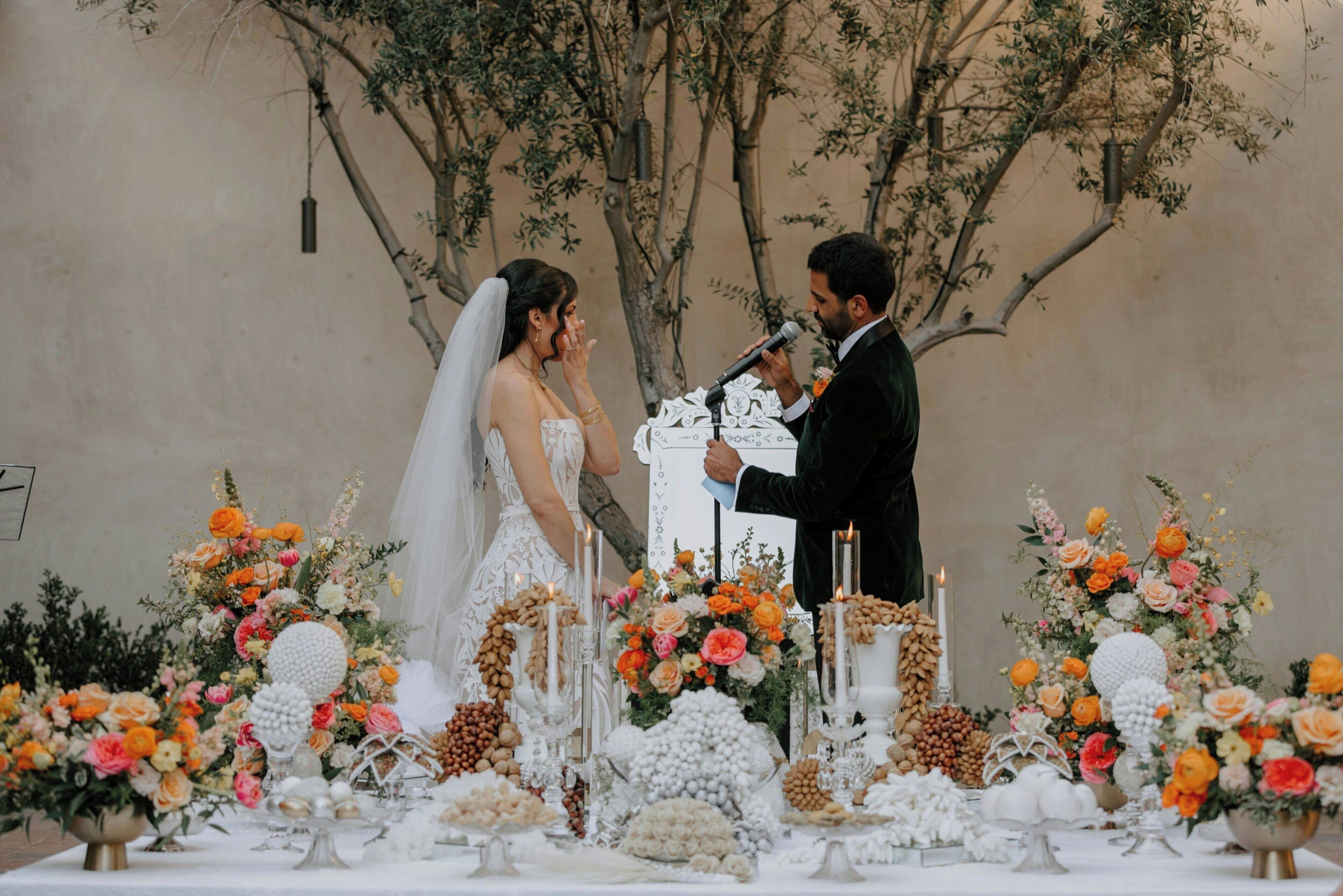 Uma cerimônia de casamento com um casal trocando votos, cercado por arranjos florais e velas.