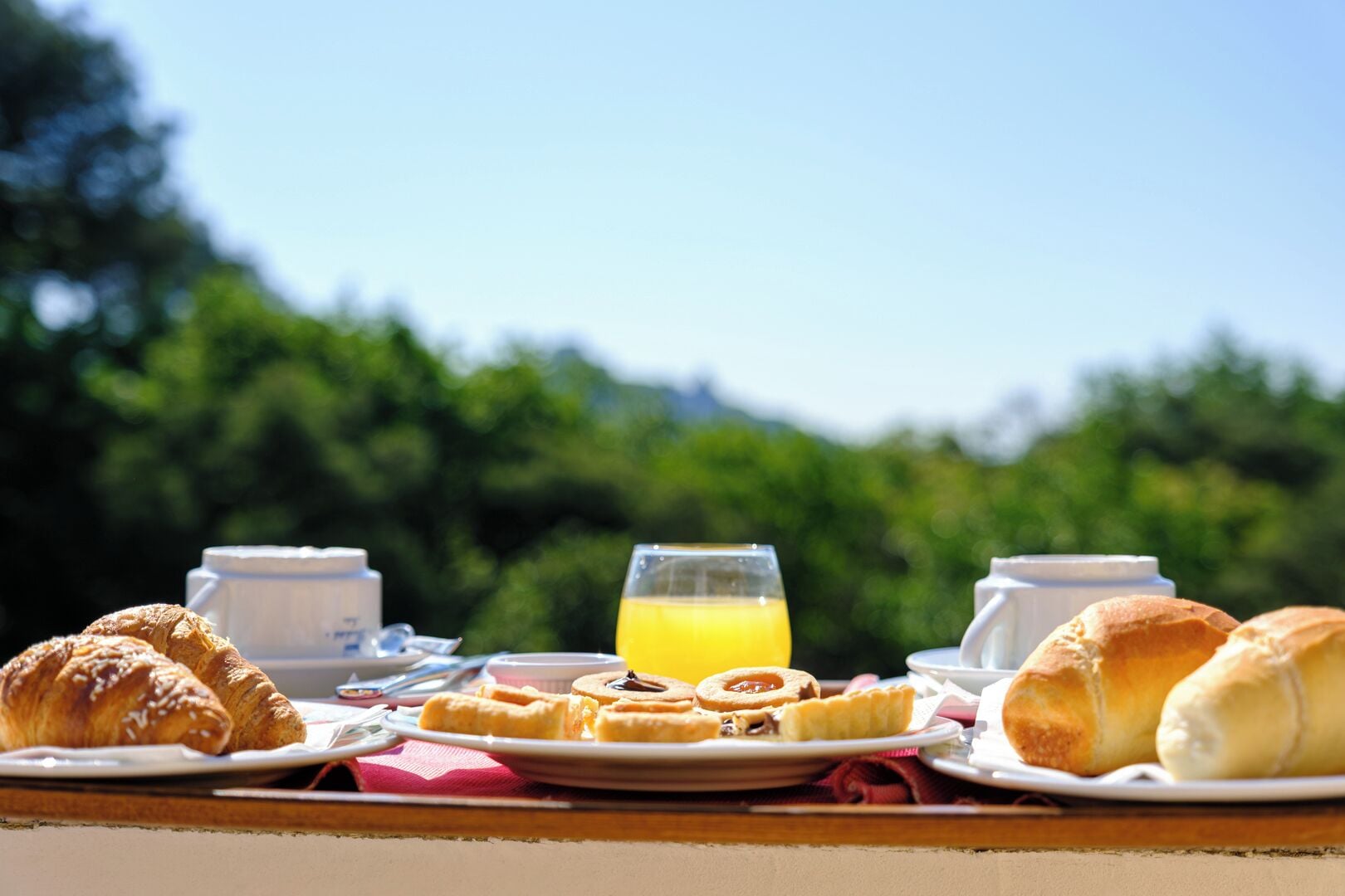 A breakfast table with pastries, a glass of orange juice, and two cups.