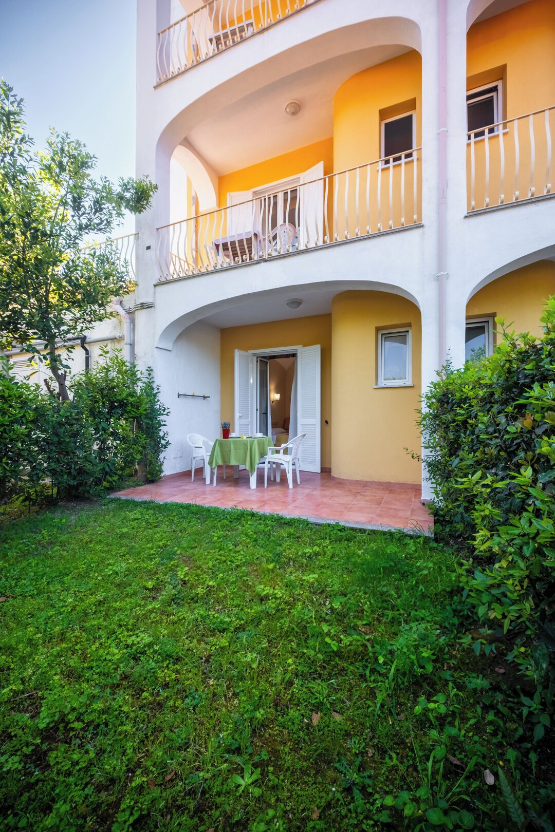 Un edificio de varios pisos con balcones, una zona de estar al aire libre techada y un jardín bien cuidado.
