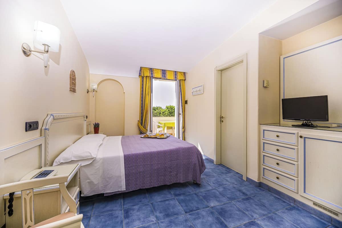 Ein Hotelzimmer mit Bett, Nachttisch, Fernseher und Blick ins Grüne.