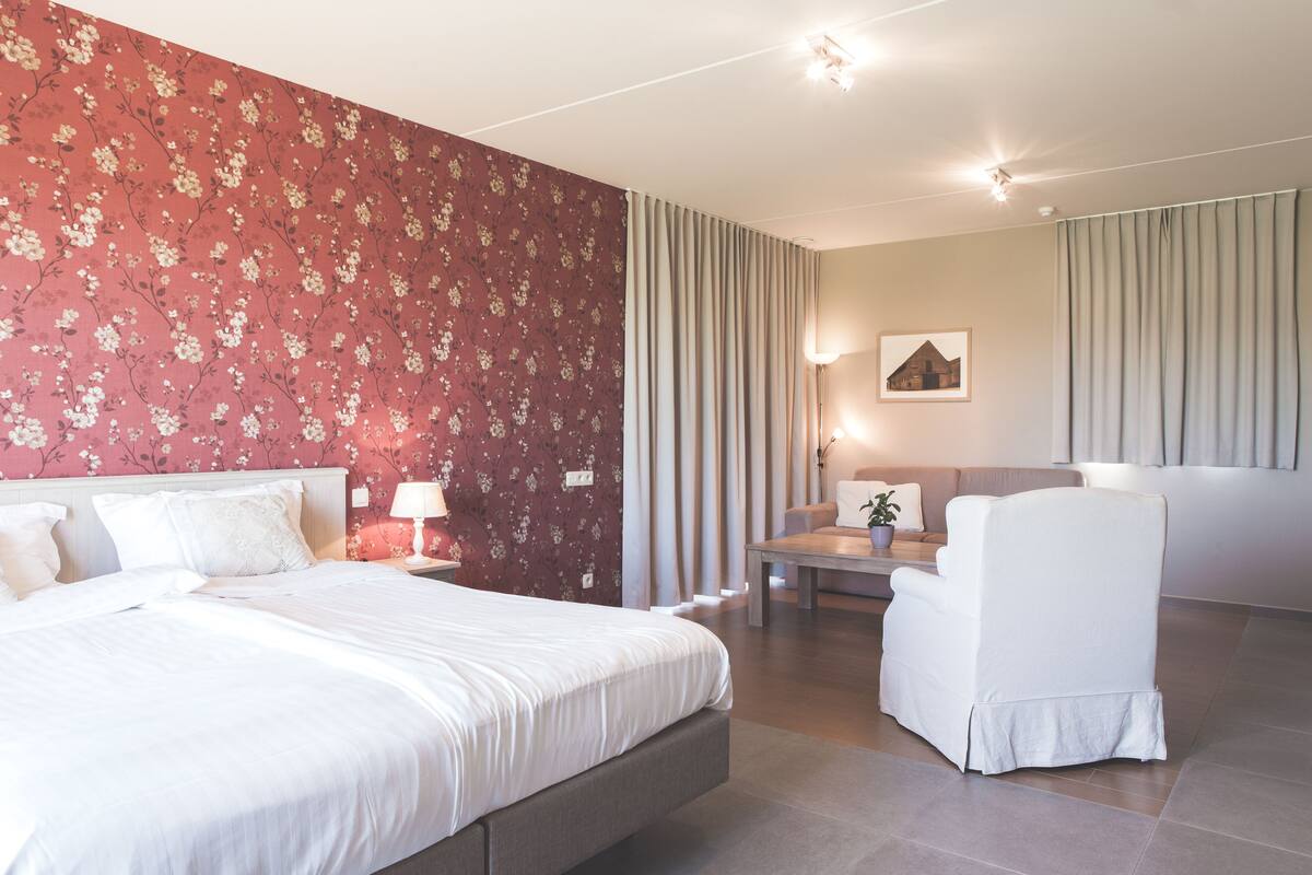 A hotel room with a large bed, a seating area with a table and chairs, and a wall with a floral pattern.