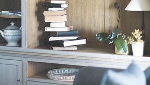 A living room with a wooden cabinet, a stack of books, a lamp, and a potted plant. - B&B Nieuwhof (Gistel)