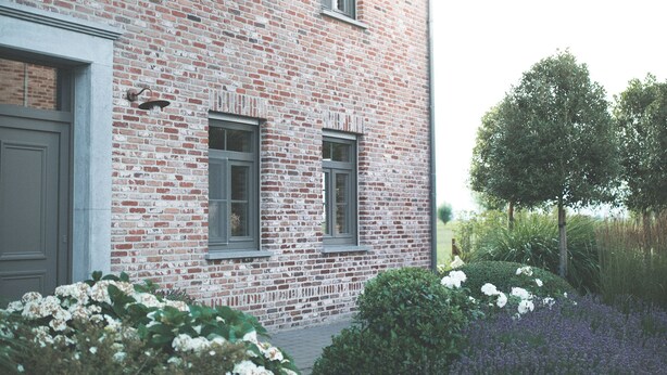 A brick building with three windows and a door, surrounded by a garden with white and purple flowers. - B&B Nieuwhof (Gistel)