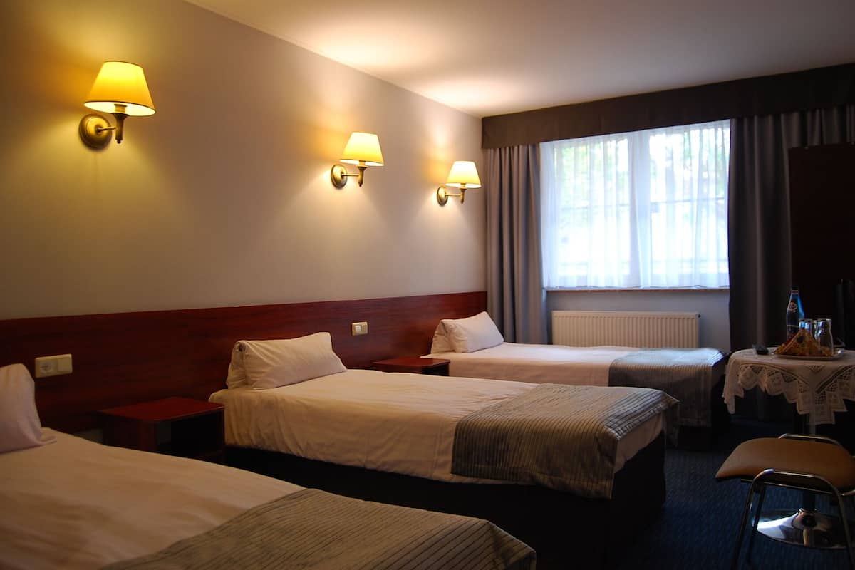 A hotel room with three single beds, a small table with a bottle and glasses, and a chair.