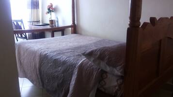 Una habitación pequeña con cama individual, cabecera de madera, mesita de noche con una botella de agua y una silla.