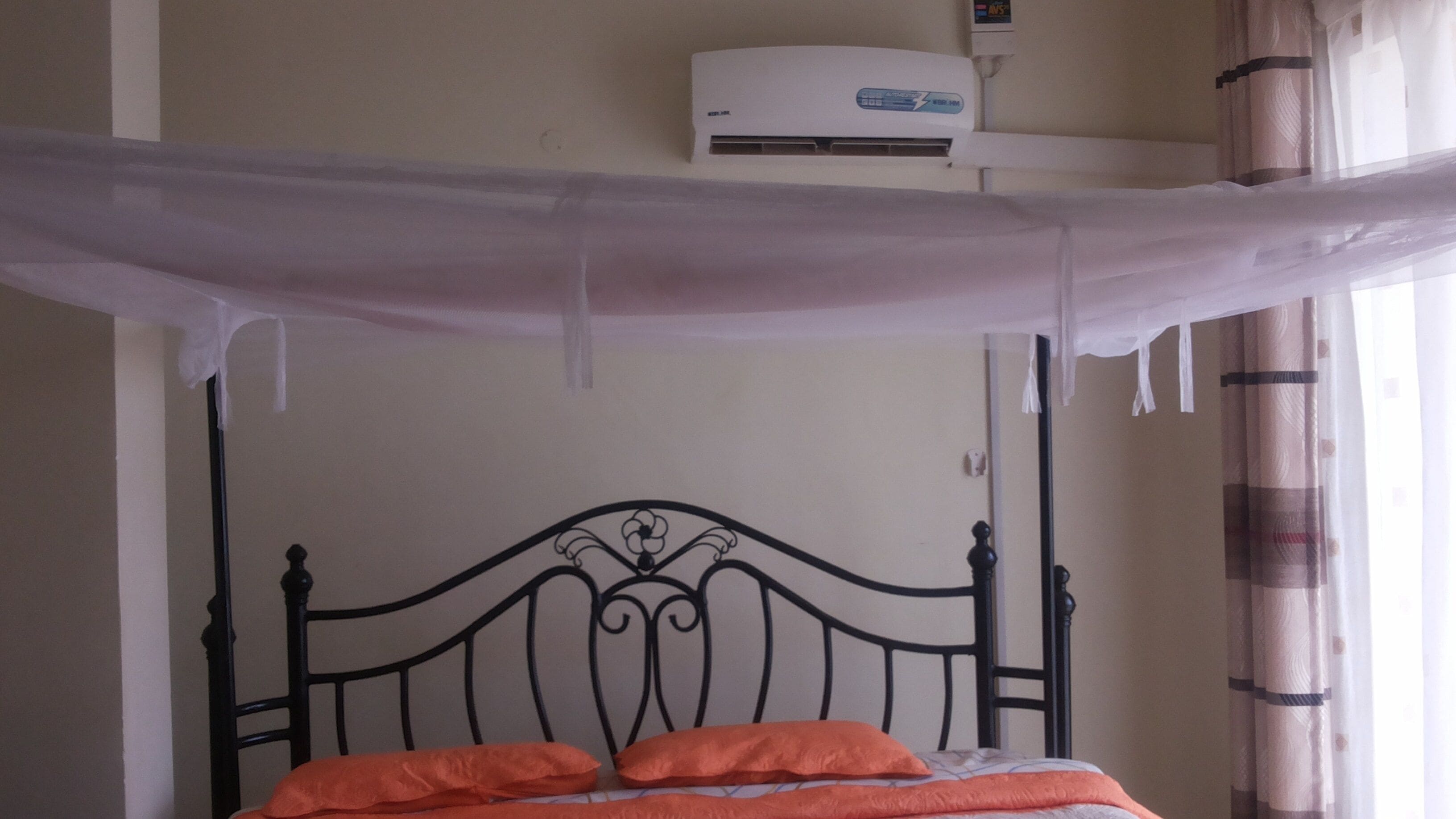 A bed with an orange blanket, a white canopy, and a wall-mounted air conditioner.
