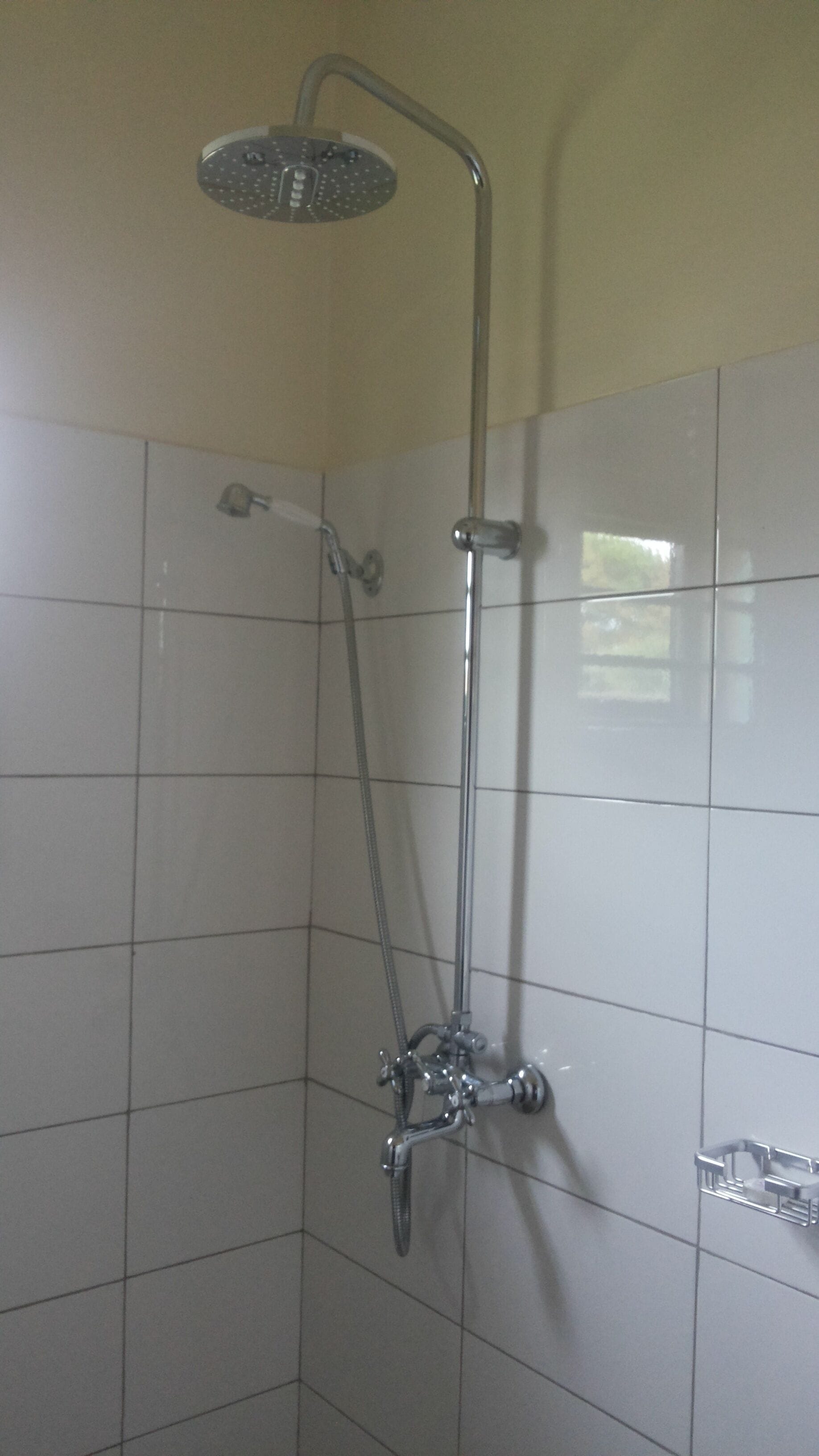 A shower with a handheld showerhead and a wall-mounted faucet.
