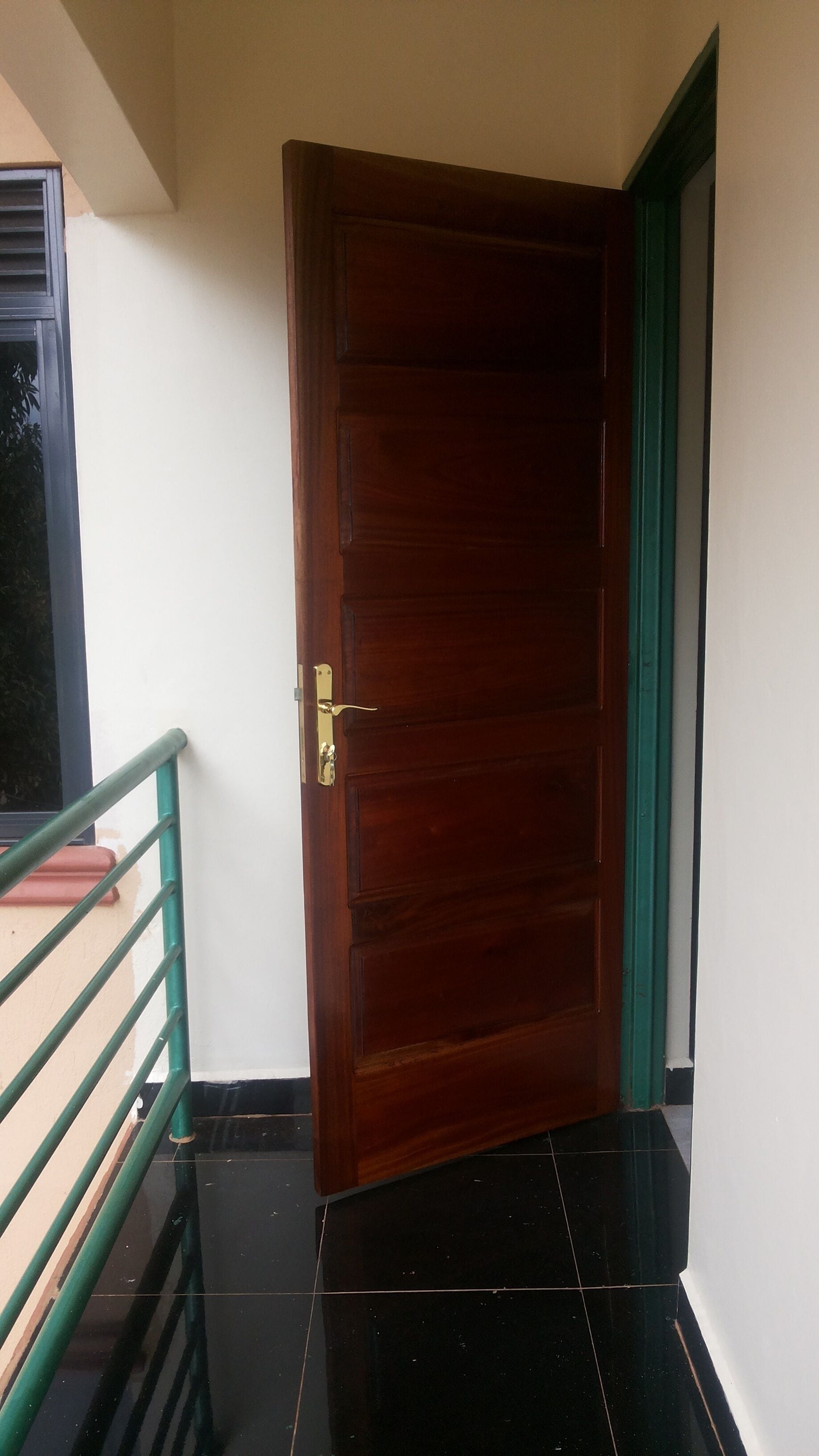Una puerta de madera con manija de latón, baranda de metal verde y suelo de baldosas negras.