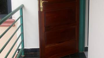 Una puerta de madera con manija de latón, baranda de metal verde y suelo de baldosas negras.