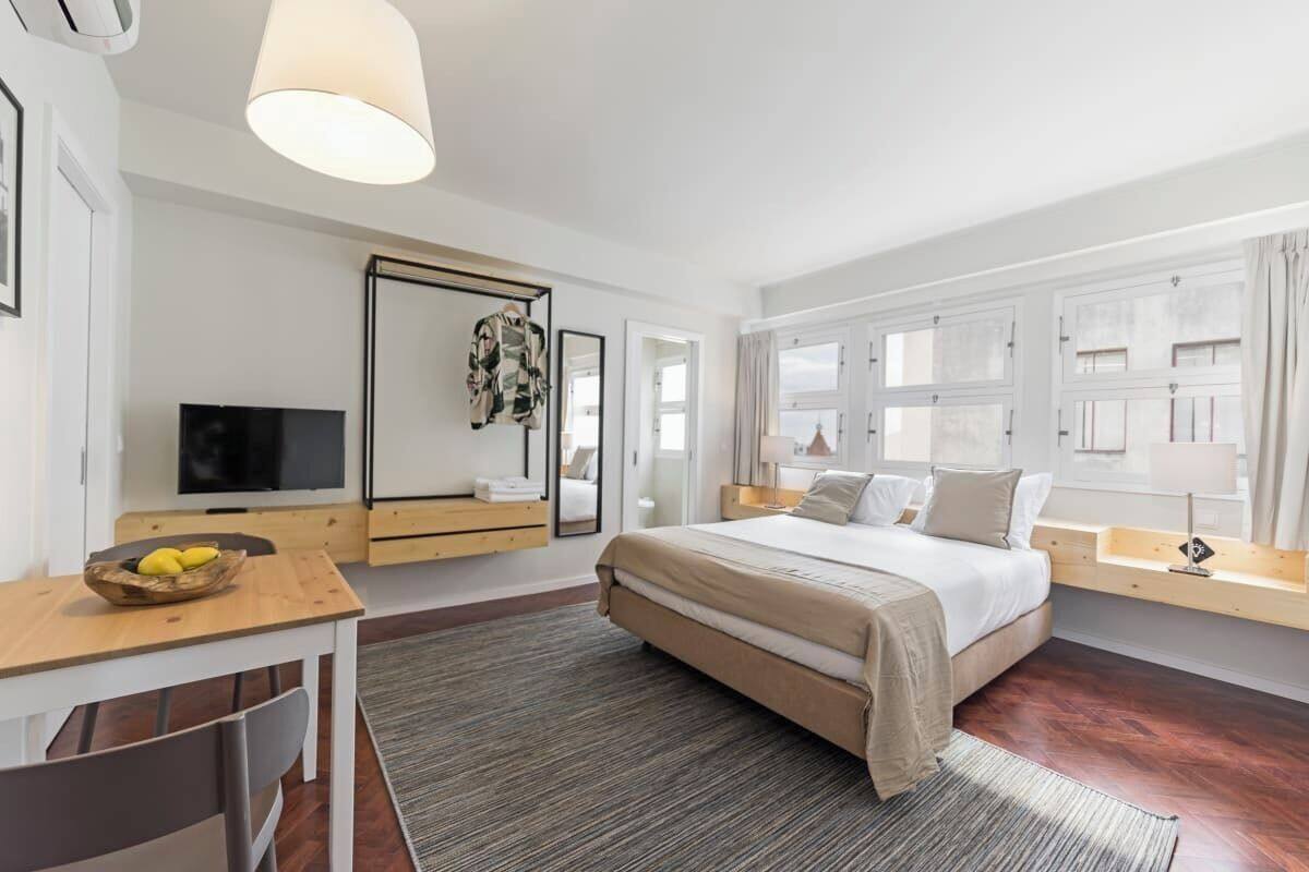 Ein modernes Hotelzimmer mit einem großen Bett, einem Schreibtisch mit Stuhl, einem Fernseher und einem Vorhangfenster.