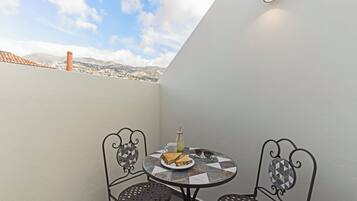 Un petit balcon avec une table et deux chaises, un sandwich, un verre de jus de fruits et une bouteille d’eau.