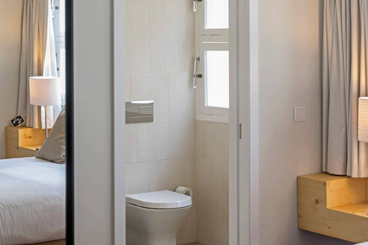 A hotel room with a bed, a toilet, and a wooden shelf.