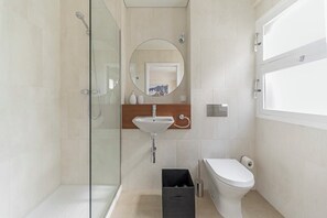 Ein modernes Badezimmer mit Duschkabine aus Glas, einem Waschbecken mit Holzplatte, Toilette und Spiegel.