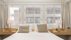 Una habitación de hotel con una cama grande, dos mesitas de noche y tres ventanas con cortinas.