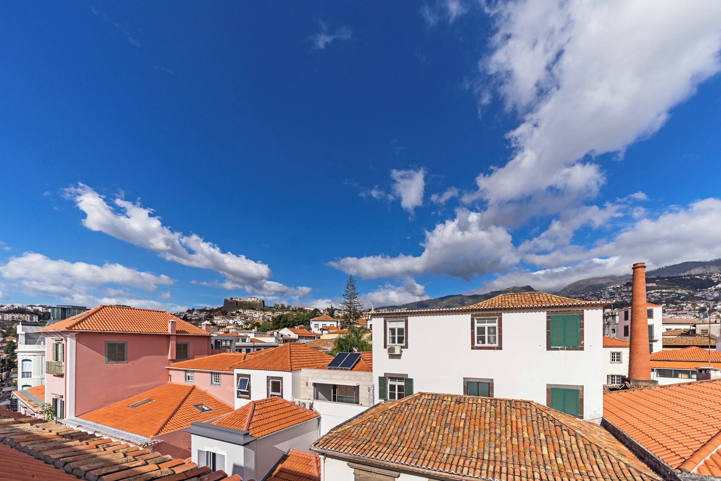 Un pueblo costero con edificios de tejas color terracota, una chimenea destacada y un cielo azul despejado.