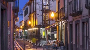 Una calle estrecha flanqueada por edificios, con mesas al aire libre en un café y un sendero adoquinado.