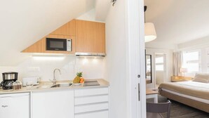 Cocina compacta con microondas, tostadora y lavabo, junto a una cama con vistas al exterior.