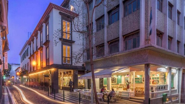 Vista de la calle de un edificio de varios pisos, con un restaurante en la planta baja y terraza.