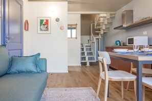 A modern living room with a sofa, a dining table with chairs, a staircase, and a kitchen area with a microwave.