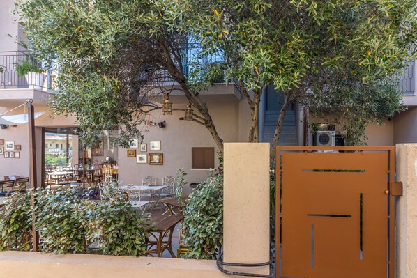 An outdoor seating area with tables and chairs, surrounded by greenery and a tree.