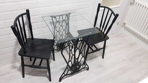A small dining area with a glass table and two black chairs, set against a white wall with a radiator. - 1930 NINETEEN THIRTY (Gijón)