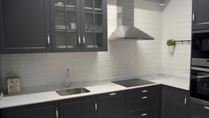 A modern kitchen with dark cabinets, a stainless steel sink, and a built-in oven. - 1930 NINETEEN THIRTY (Gijón)