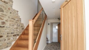 Un escalier en bois, doté d’une rampe en verre, mène à une pièce dont l’un des murs est en pierre.