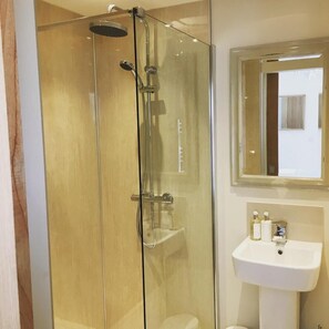 Ducha envuelta en vidrio con cabezal de ducha de mano y grifo de pared.