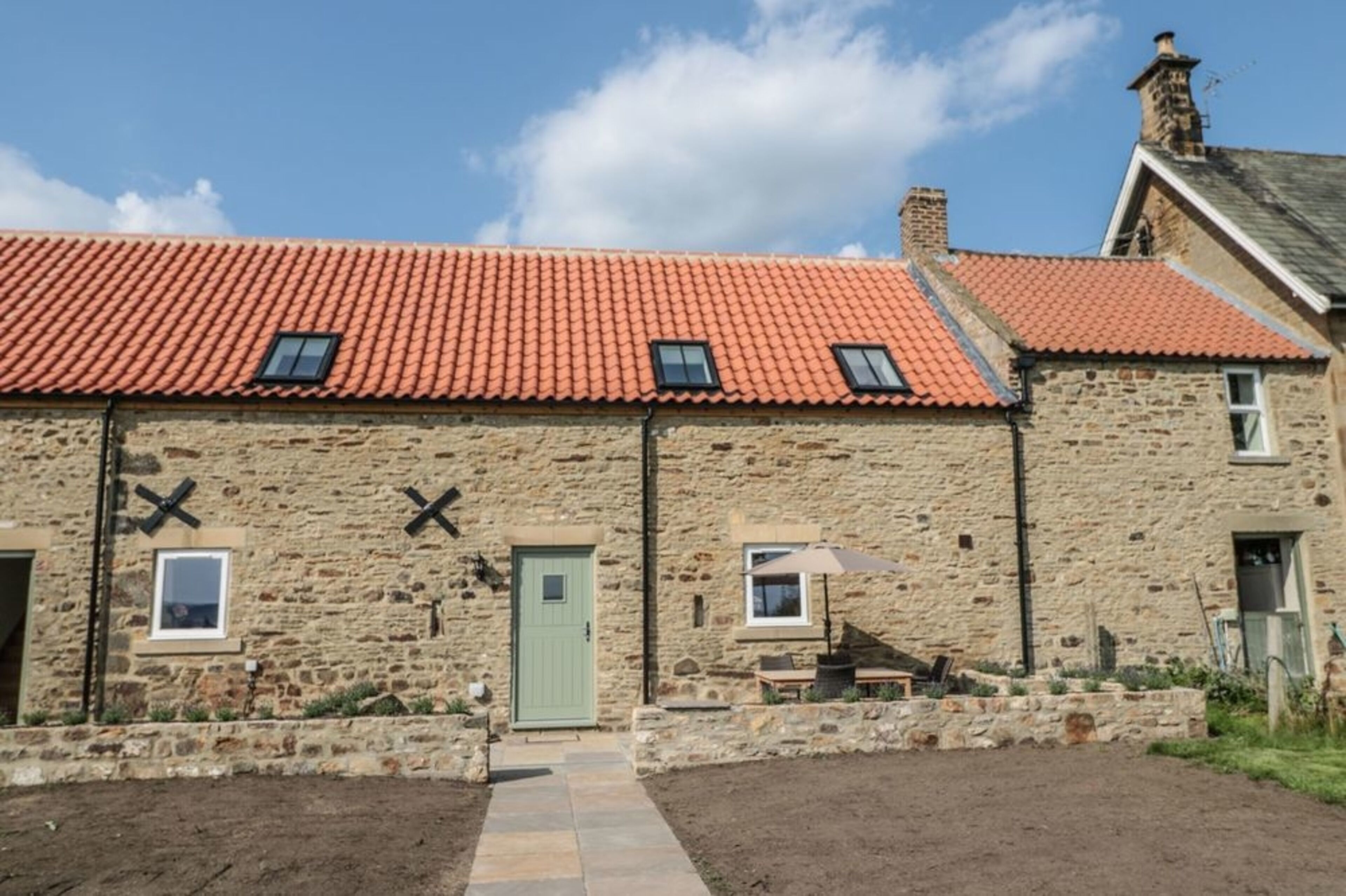 A stone building with a red-tiled roof, a green door, and a small window.