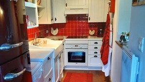 Une cuisine de taille réduite avec des meubles blancs, un pare-feu rouge en carreaux, un tapis rouge et un réfrigérateur rouge.
