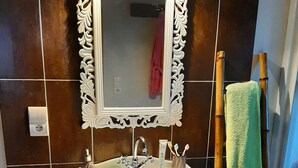 Une salle de bain avec un lavabo sur pied, un grand miroir blanc à motifs, une serviette verte et un escabeau en bambou.