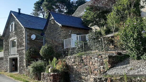 Une maison en pierre avec un toit en pente, un petit balcon et un mur en pierre agrémenté d’un élément décoratif à eau.