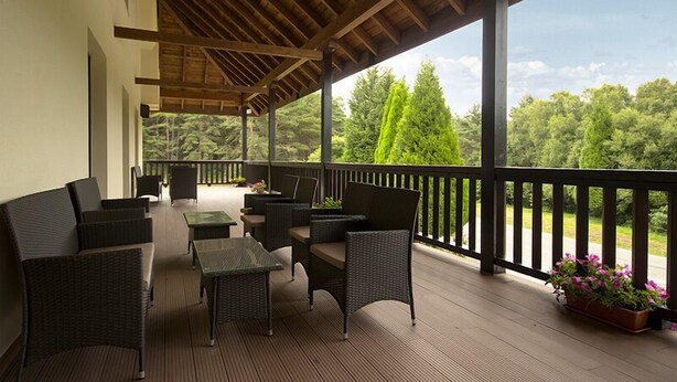 A covered outdoor seating area with wicker furniture and a view of the surrounding greenery. - Complejo O Piñeiral (Fonsagrada)