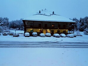A snow-covered lodge with a balcony and several cars parked in front. - Complejo O Piñeiral (Fonsagrada)