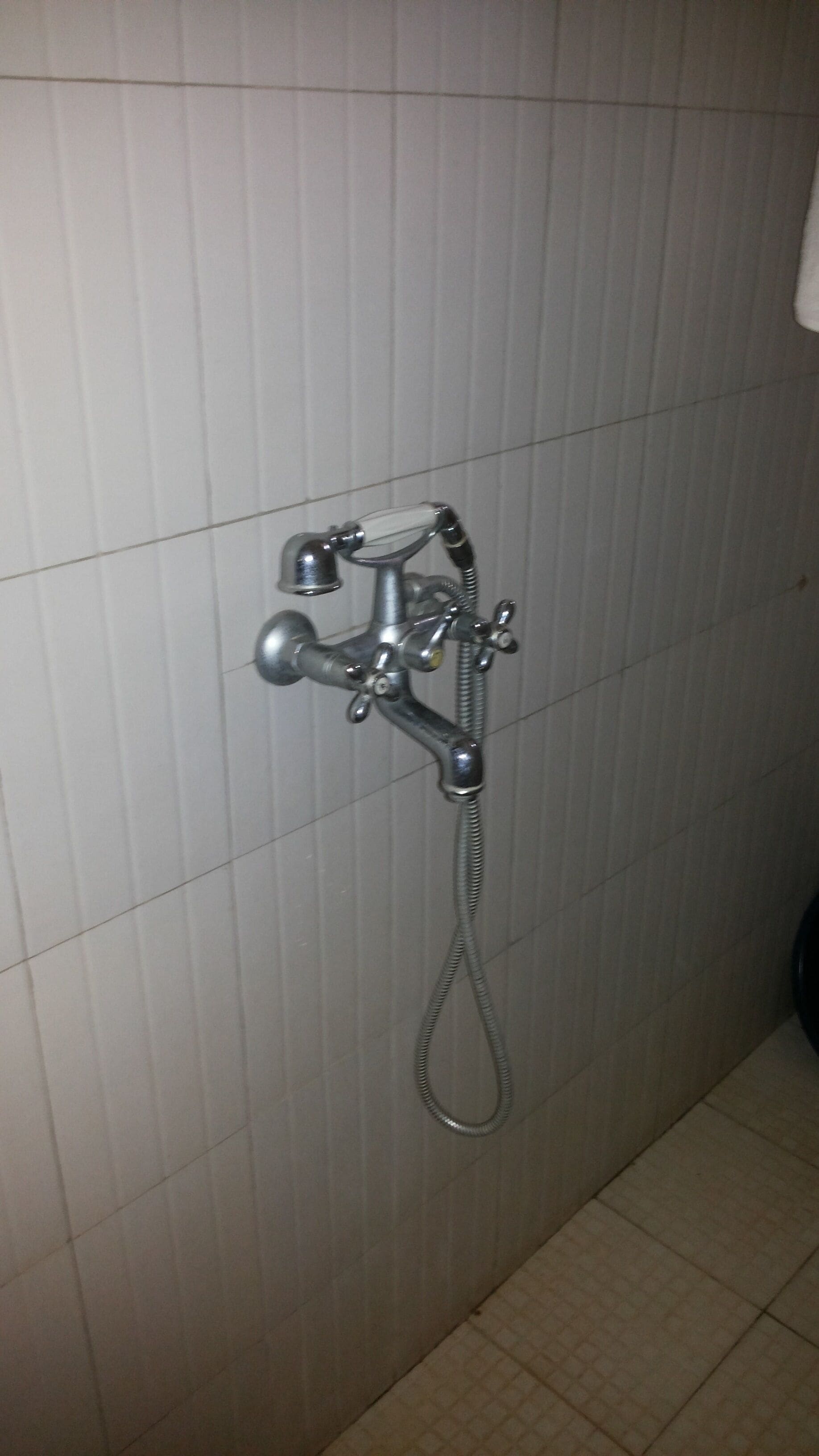 A bathroom with a shower fixture mounted on a tiled wall.