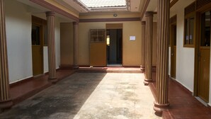A corridor with columns, a tiled floor, and a door leading to another room. - Hotel Bucolic Heritage (Adjumani)