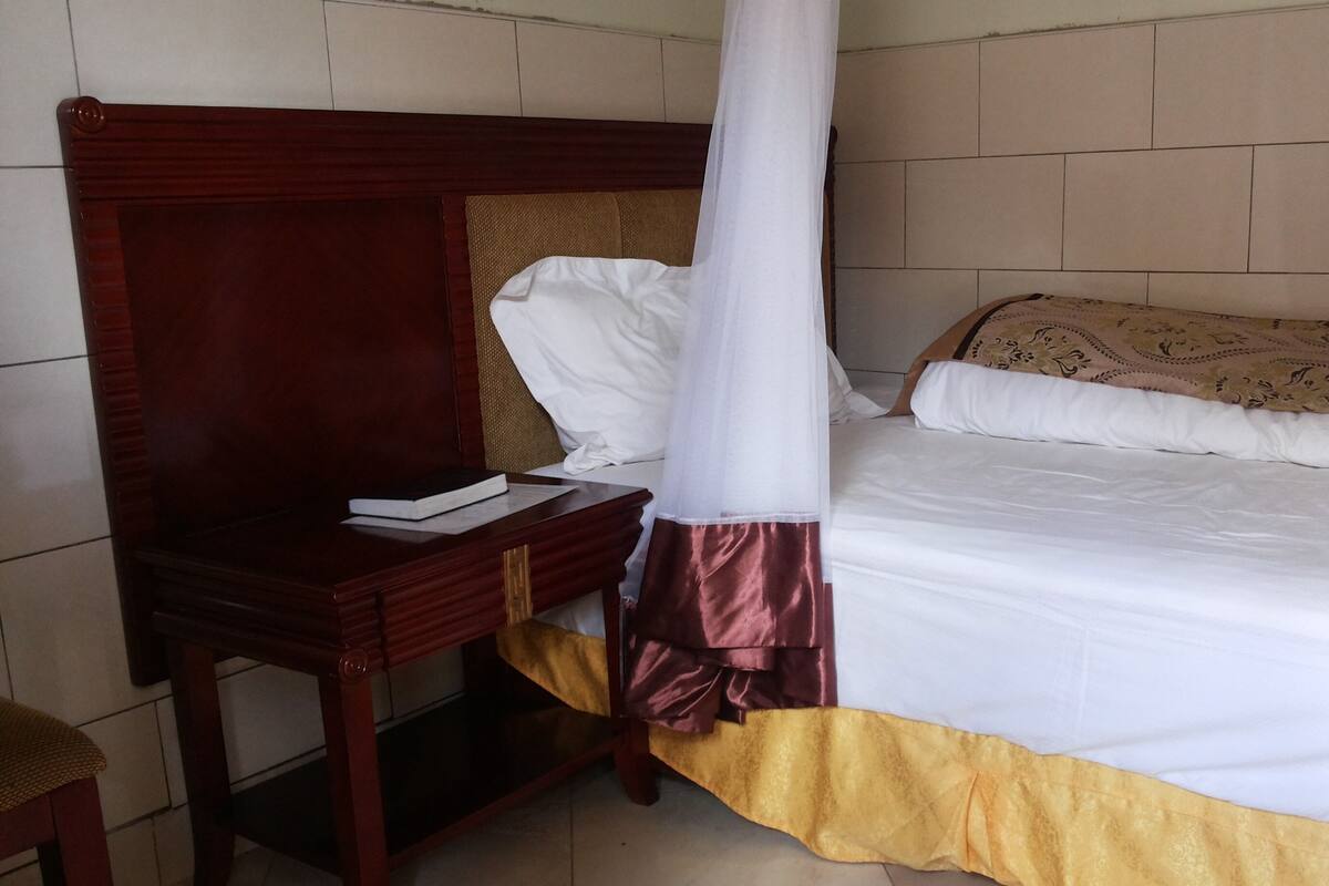 A single bed with a canopy, a bedside table with a book, and a chair.
