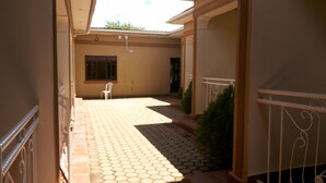A covered outdoor area with a tiled floor, a white plastic chair, and a small green plant. - Hotel Bucolic Heritage (Adjumani)