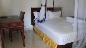 A bed with a canopy, a bedside table, and a chair in a hotel room. - Hotel Bucolic Heritage (Adjumani)