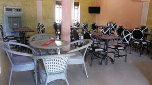 A dining area with wicker chairs and tables, a television mounted on the wall, and an air conditioning unit. - Hotel Bucolic Heritage (Adjumani)