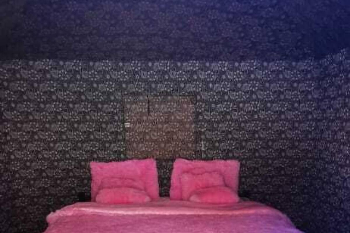 A bedroom with a pink bedspread, two pillows, and a hanging light fixture.