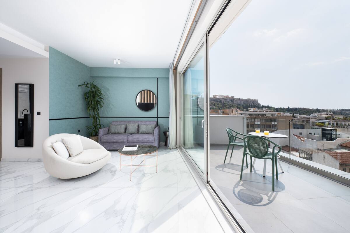 Un salon moderne avec un canapé, une table ronde et un balcon équipé de chaises.