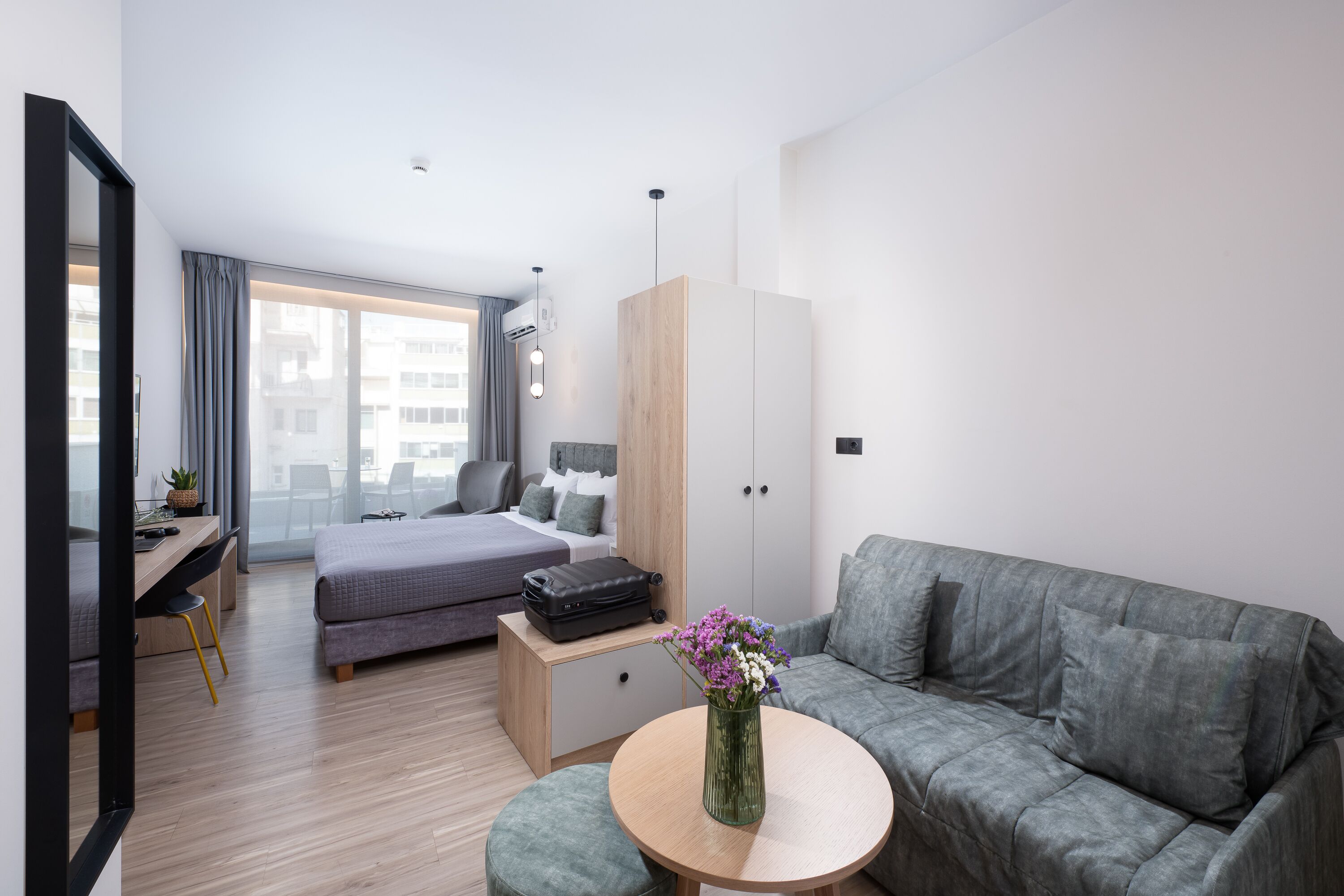 Una habitación de hotel moderna con cama, sofá, escritorio y un ventanal grande.