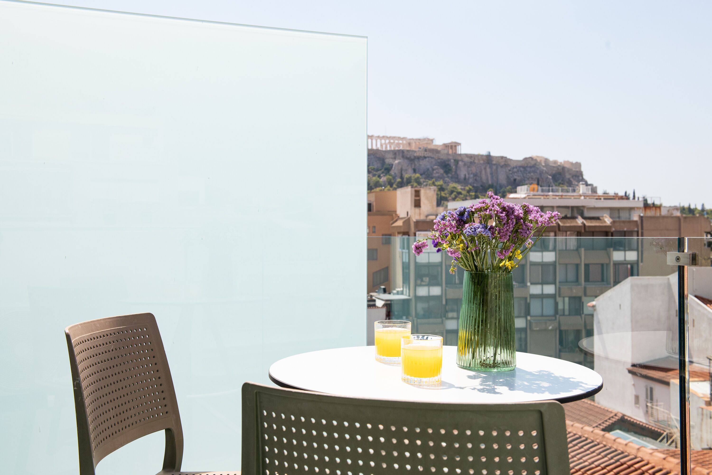 A balcony with a table, two chairs, a vase with flowers, and two glasses of orange juice.