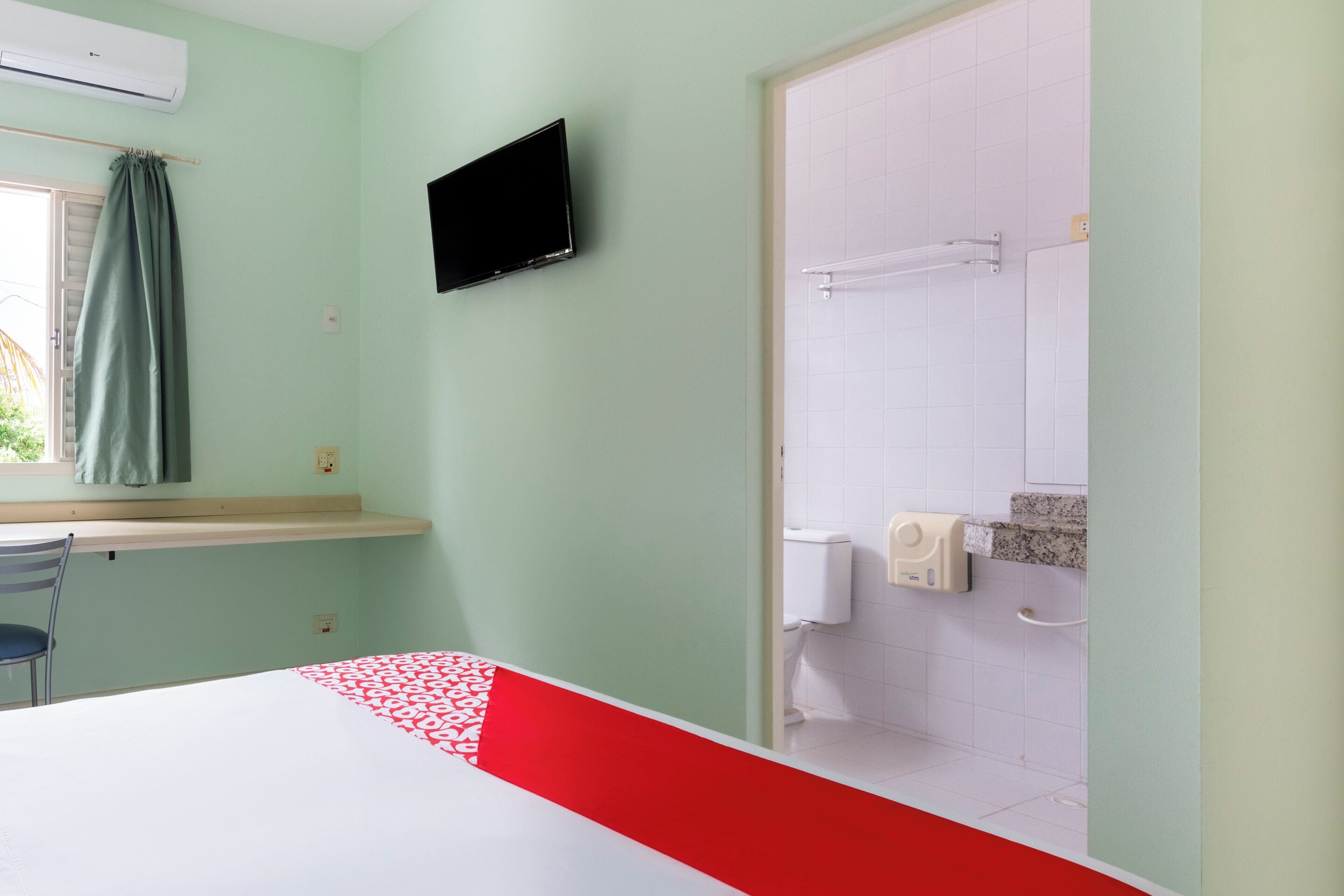 Une chambre comprenant un lit, un téléviseur fixé au mur, une fenêtre avec un rideau et un espace douche avec un porte-serviettes.